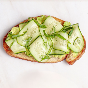 A slice of bread, one topped with tahini and sliced cucumber