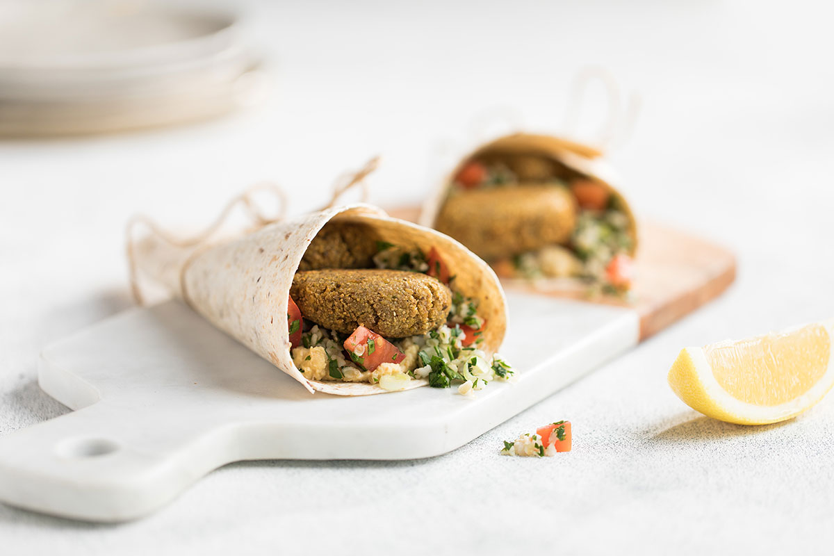 Image of two falafel hummus and tabouli wraps on a white cutting board with a lemon wedge to serve