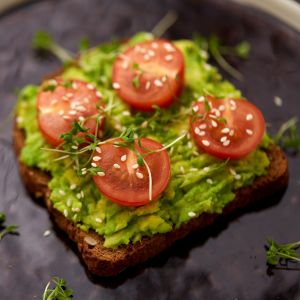 Smashed avocado, four slices of tomato on wholegrain toast with a sprinkling of sesames on top