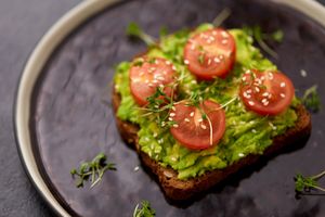 Smashed avocado, four slices of tomato on wholegrain toast with a sprinkling of sesames on top
