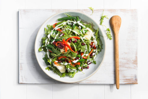 Image of the bean salad in a white bowl shot from above on a white wooden chopping board with a wooden spoon to serve