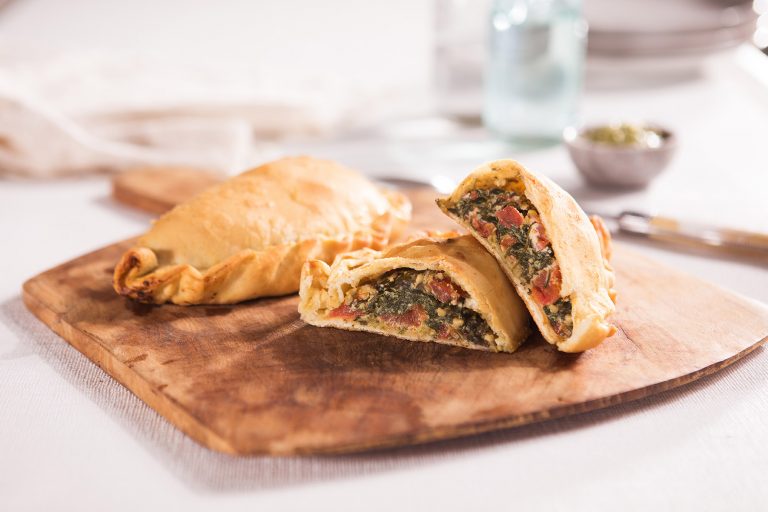 Image of two calzones one sliced in half to see the filling on a wooden chopping board with a glass of water in the background