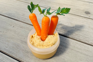 A small pottle of hummus with three mini carrots sticking out of it