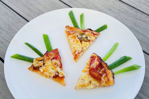 Pizza cut into wedges in the shape of carrot with three sprigs of green onion out of the tops
