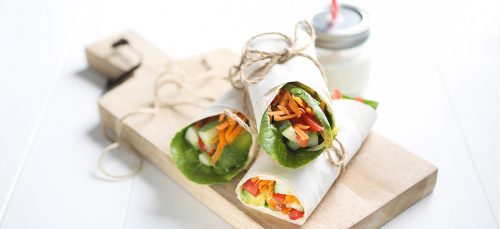 Image of three cheese and avocado salad wraps on a wooden chopping board with a milk jar with straw on the side