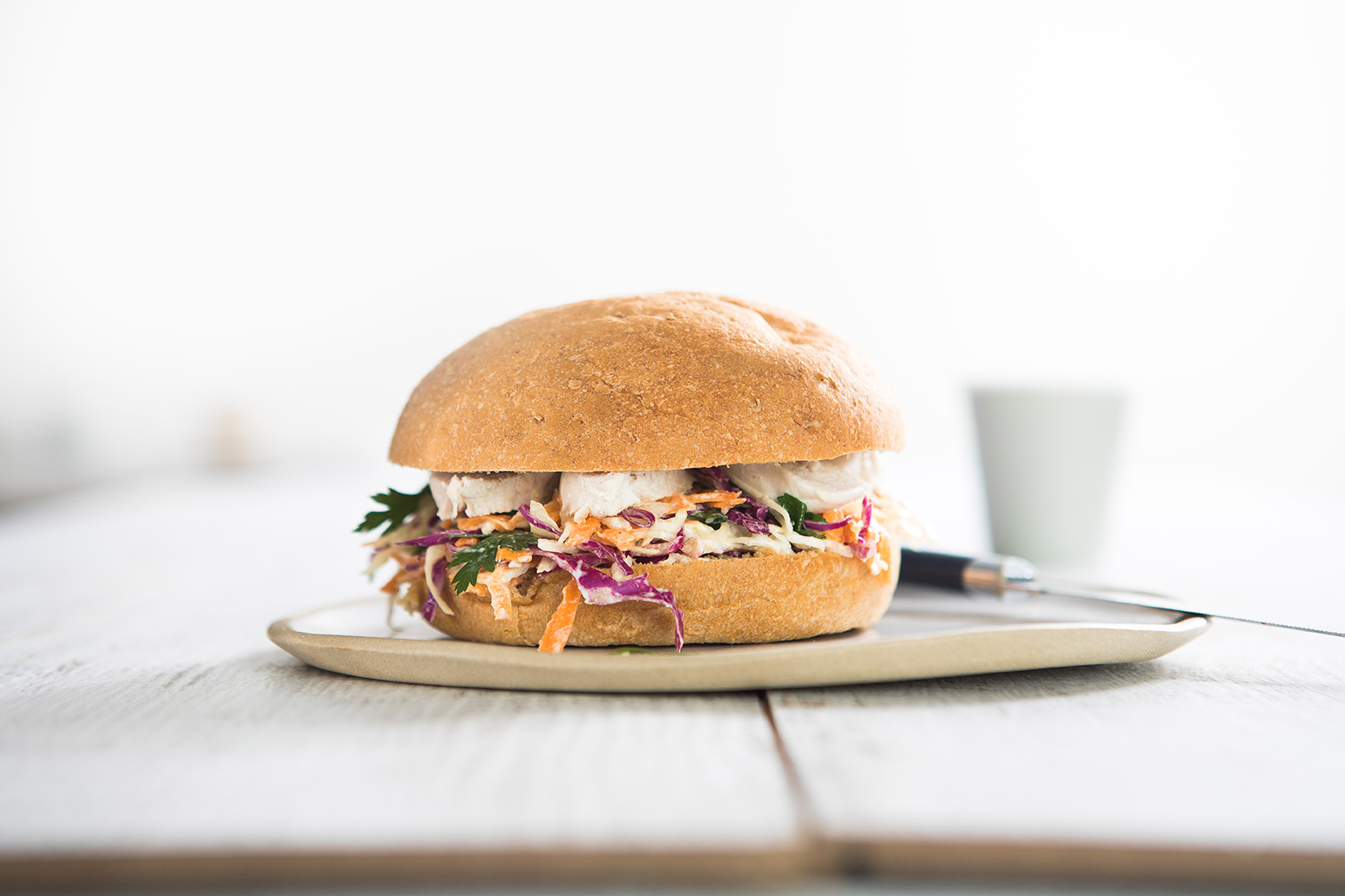 Image of chicken coleslaw roll on a large plate with a cup and knife in the background