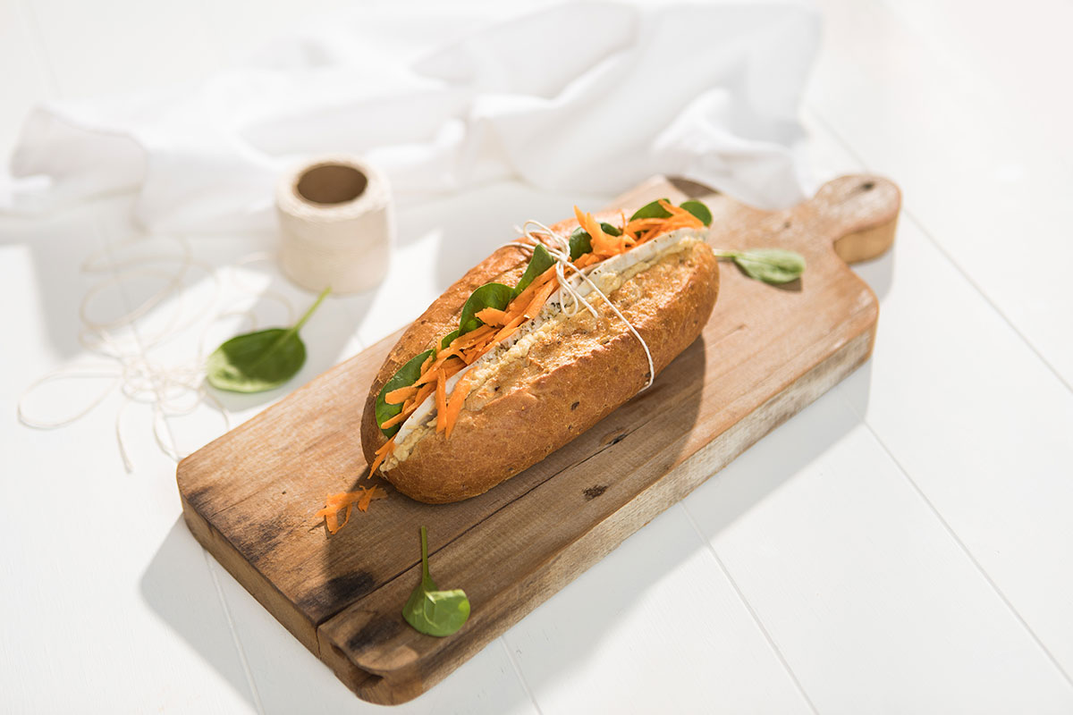 Image of a multigrain wholemeal roll with chicken, hummus and carrot filling served on a wooden cutting board and held together with twine