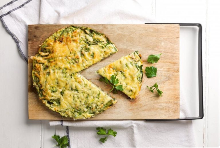 Crustless salmon quiche with a piece cut out and sitting alongside, served on a timber board with a white napkin underneath. 