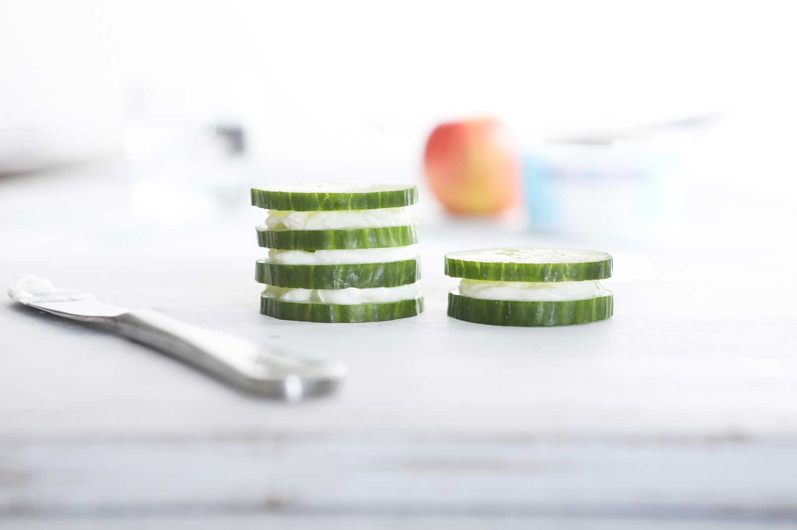 Slices of cucumber stacked with cream cheese in between and a knife for spreading cream cheese