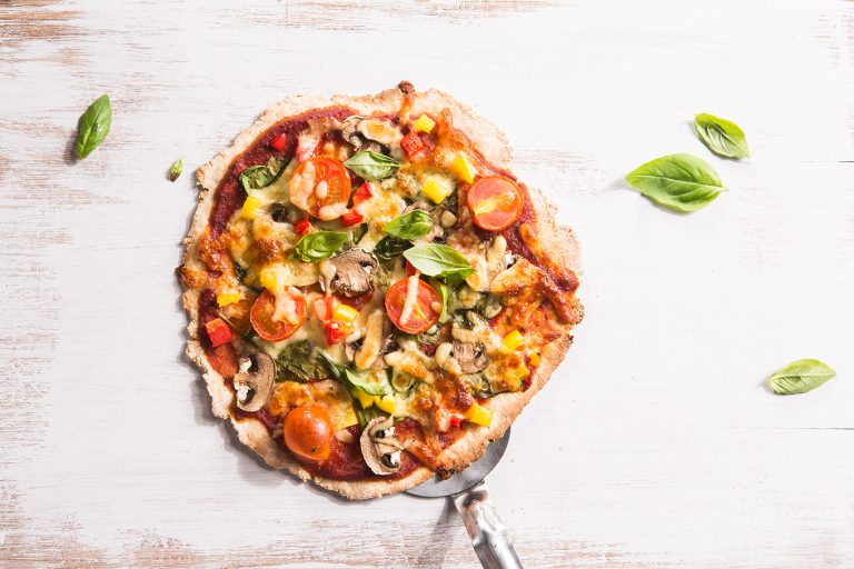 Image of an easy home made pizza on a white cutting board sprinkled with basil on top and the side and a serving knife, shot from above