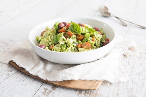 Image of Easy Pasta Salad in a large white bowl on a white cloth napkin sitting on a chopping board with a serving spoon in the background