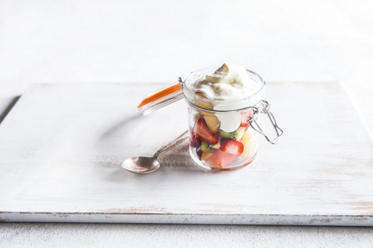Strawberry, apple, kiwi fruit and watermelon chunks in a glass jar topped with yoghurt.