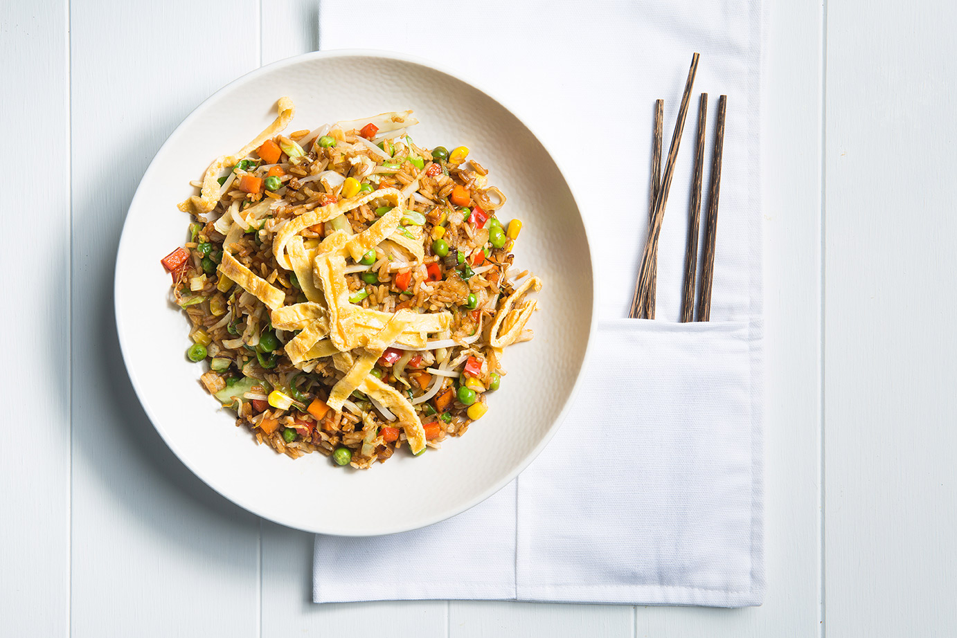 Image of a cooked fried rice served in a large open white bowl on a plain white napkin with four wooden chopsticks on the side