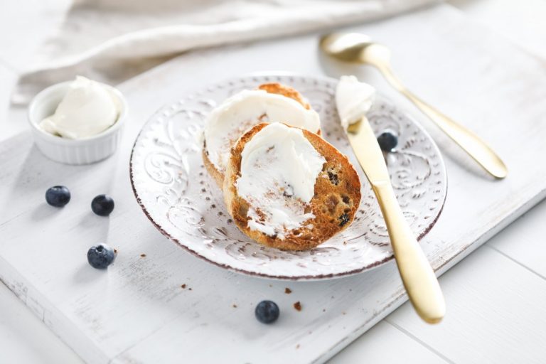 Two pieces of toasted muffin on a white plate with scattered blueberries