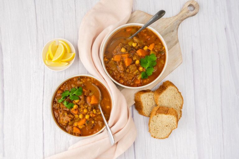 2 round bowls containing beef, lentil and chickpea soup. In front are 3 slices of bread stick and at the back a round bowl containing lemon segments. A napkin sits between the bowls of soup.