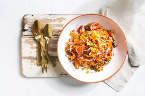 Image of an Indian salad in a white bowl with orange trim on a wooden chopping board with gold cutlery on the side for serving