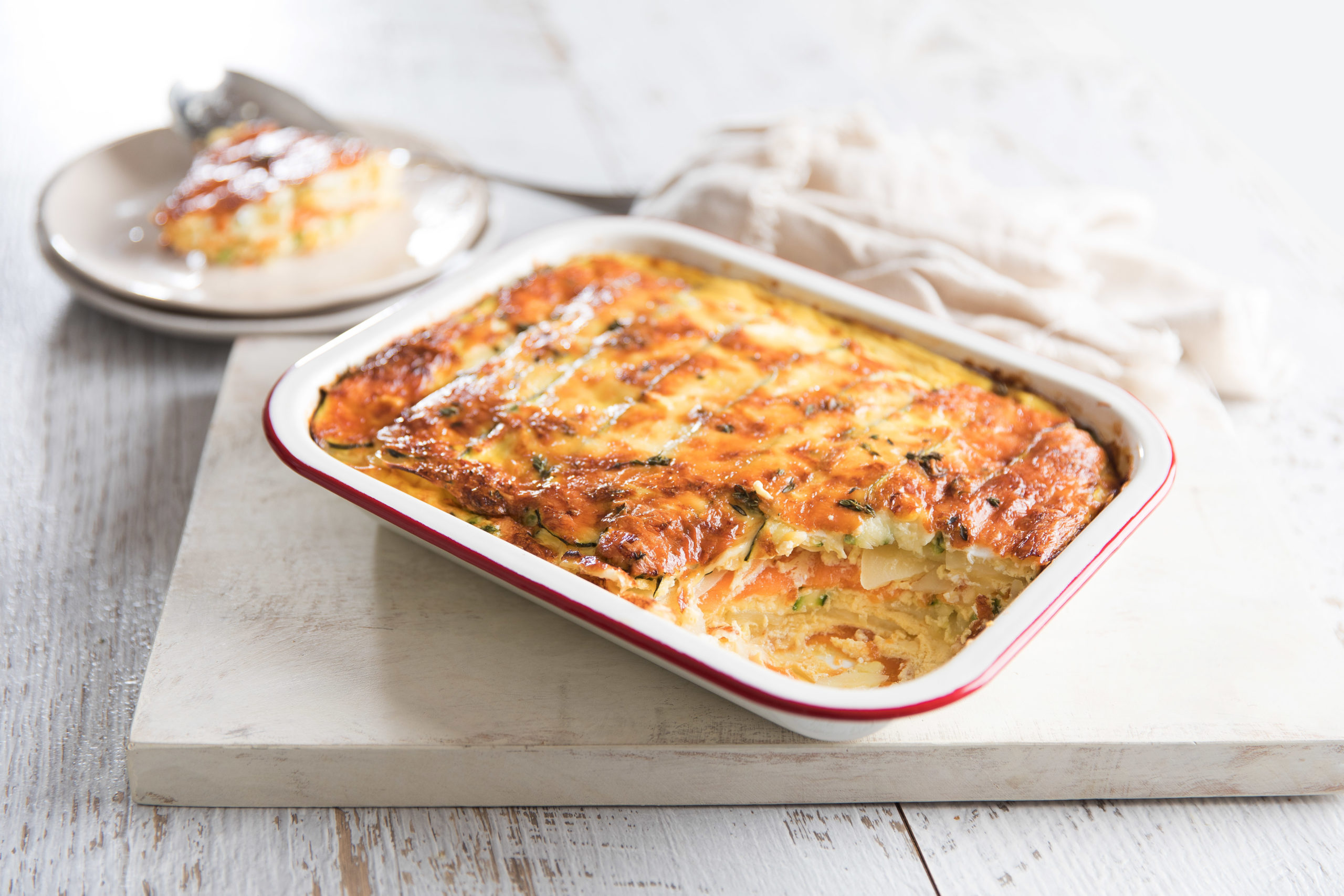 A rectangular enamel dish containing mixed potato bake on a white board