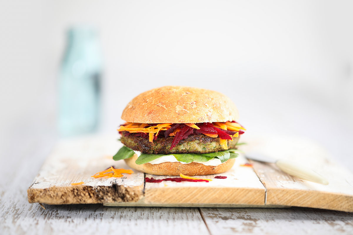 Image of a lentil pattie burger served on a wooden cutting board with a glass jug of water in the background