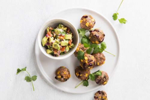 Cooked Mexican meatballs and a small bowl of salsa served on a large white serving plate with coriander sprinkled for decoration.