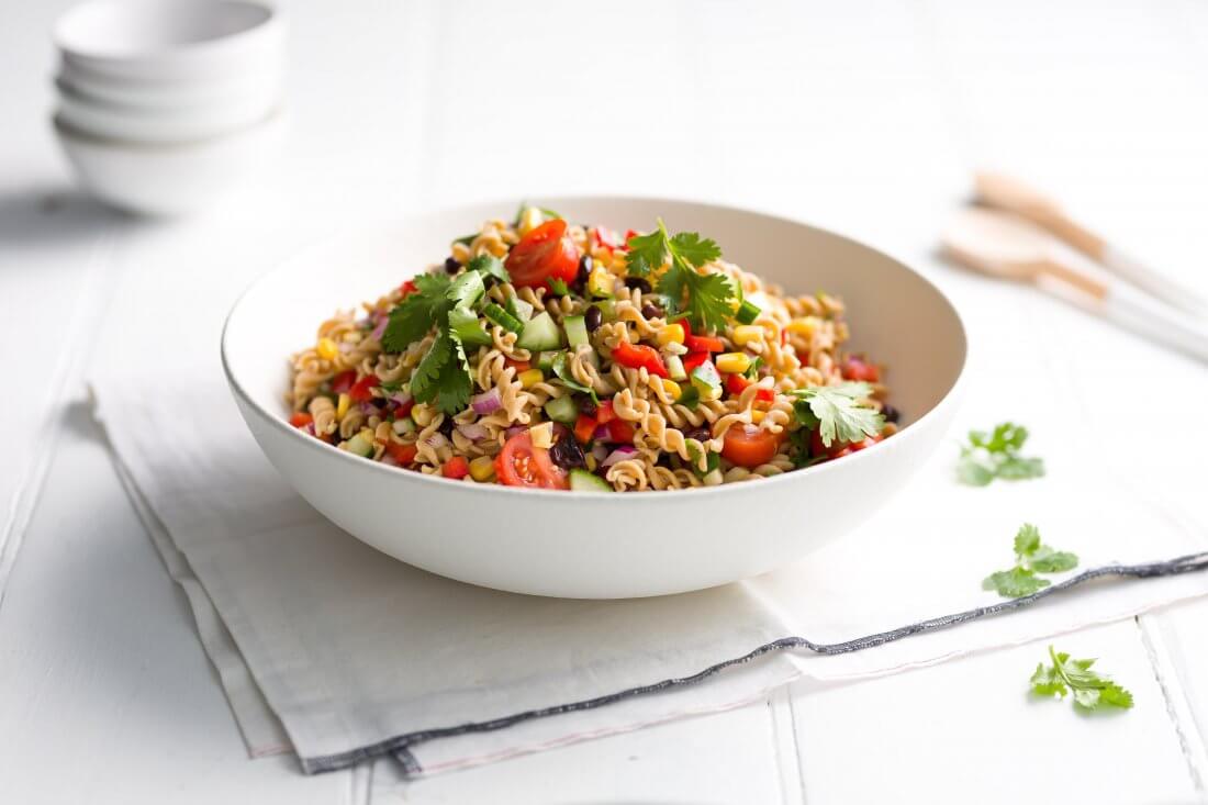 Mexican Pasta Salad in a round white bowl on a napkin with small white bowls at the back.