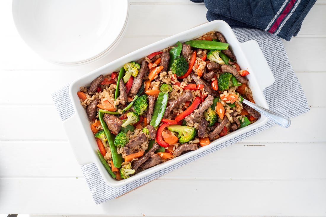 Beef and vegie rice bake in dish with plates in background