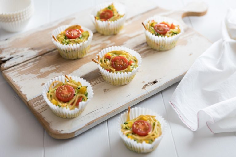 Baked noodle cakes in patty cases served on a wooden serving board.  