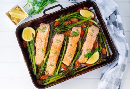 Cooked salmon and vegetables in tray with plates in background