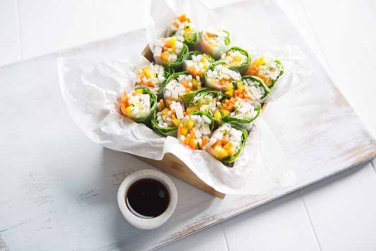 Image of rice paper rolls served in a large container with baking paper and a dipping sauce on the side