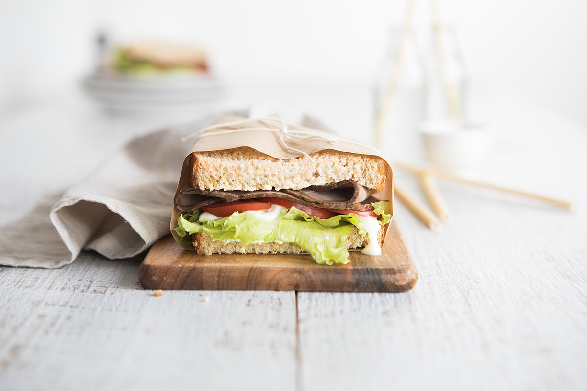 Image of a roast beef sandwich on a wooden cutting board with napkin on the side