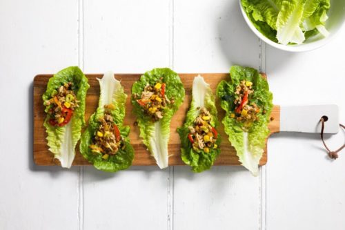 Five lettuce leaves containing a mince and vegetable mixture on a timber board