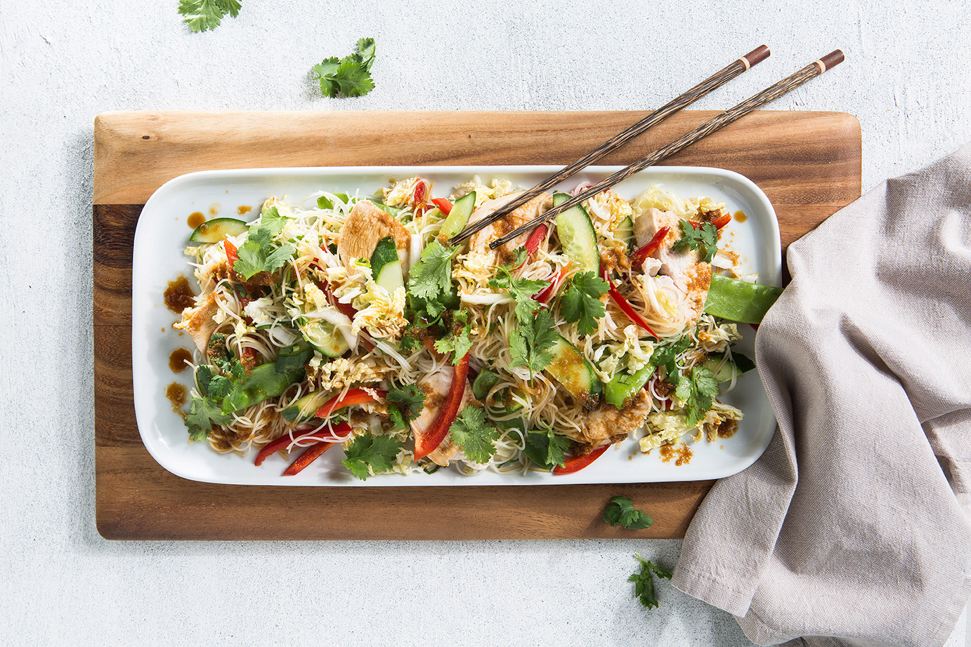 Image of soy, ginger and chicken noodle salad on a large rectangle serving platter on a wooden chopping board with chopsticks to serve