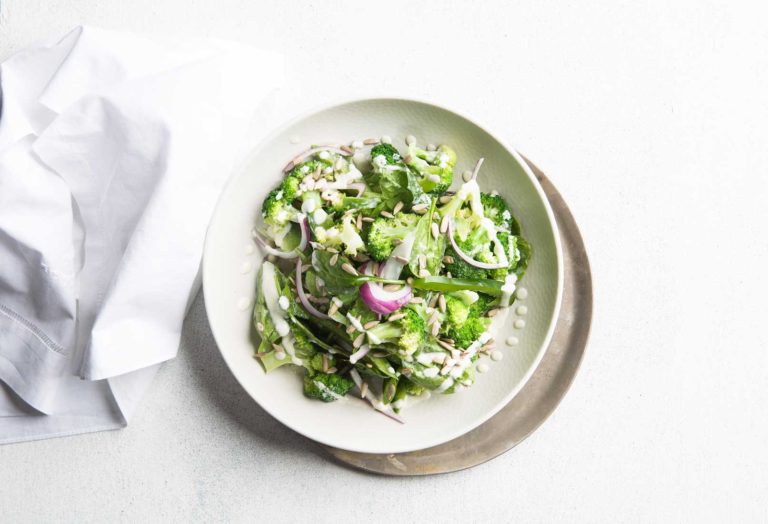 Image of spinach and broccoli salad in a large white bowl shot from above with a white cloth napkin on the side