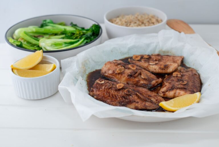 Steamed fish on plate with green vegetables and rice in the background