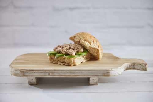 A bread roll containing tuna, sliced cucumber and mayonnaise on a timber board