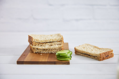 Three halves of a vegemite sandwich on a timber board with cucumber slices in the foreground