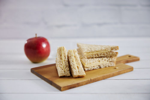 Four quarters of cheese sandwich on a timber board with a red apple in the background