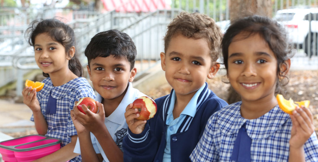 Four school children smiling while eating their fruit snack